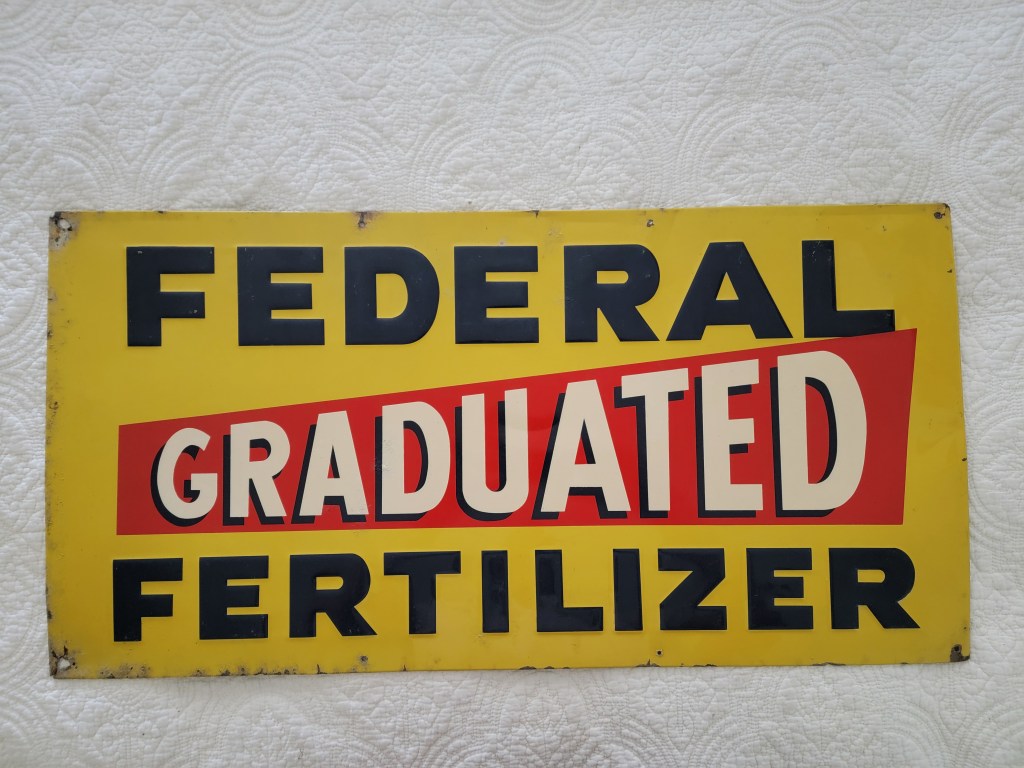 A vintage sign displaying the words 'FEDERAL GRADUATED FERTILIZER' in bold letters, with a yellow background and red accents.
