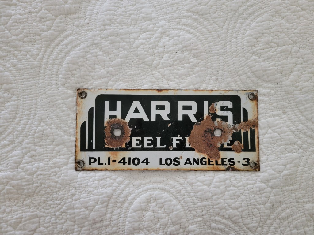 A close-up of a weathered metal nameplate that reads 'HARRIS STEEL FENCE' with visible rust spots, mounted on a textured white surface.
Vintage fence sign los angeles california