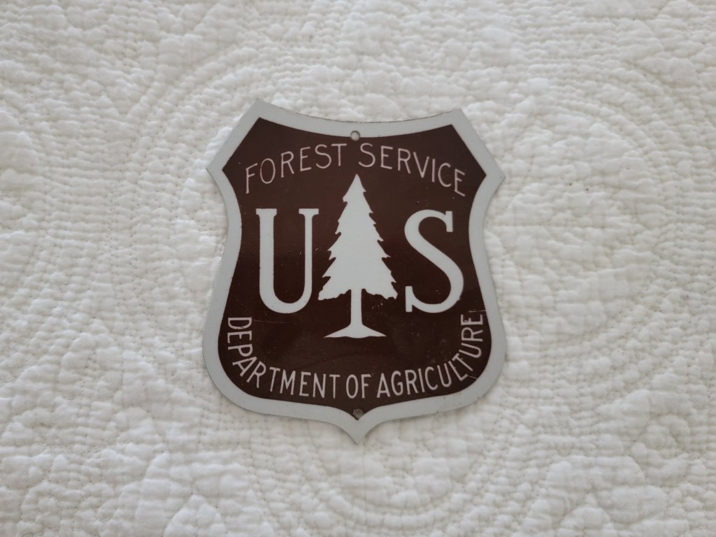 A Forest Service badge from the U.S. Department of Agriculture on a textured white background.