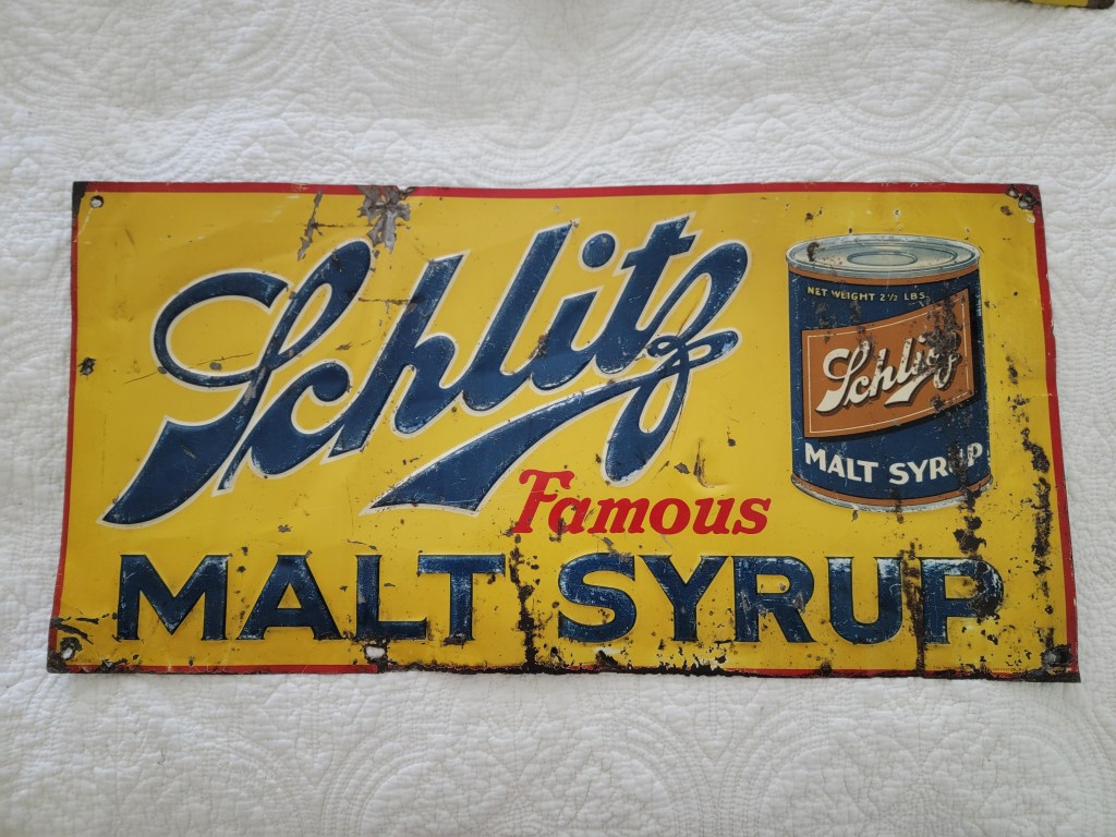 Vintage Schlitz Malt Syrup advertising sign featuring bold blue lettering on a yellow background with an image of a can. Front