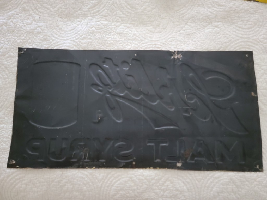 Vintage Schlitz Malt Syrup advertising sign featuring bold blue lettering on a yellow background with an image of a can. Back