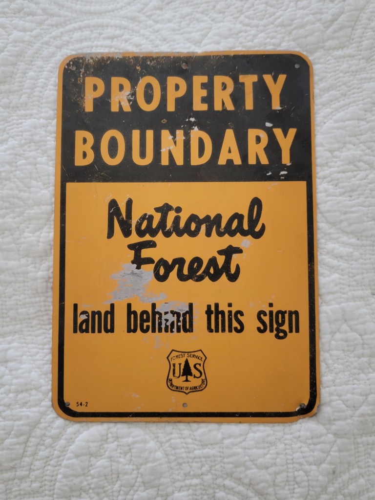 A black and yellow sign that reads 'PROPERTY BOUNDARY National Forest land behind this sign' with the U.S. Forest Service emblem at the bottom.