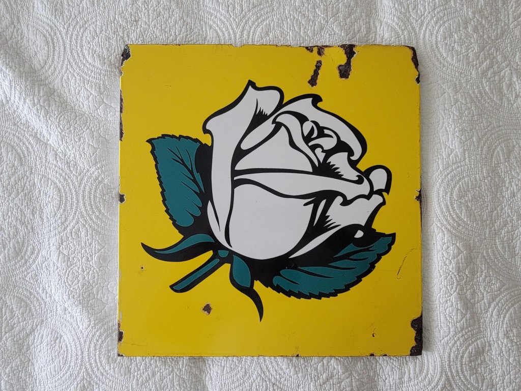 A stylized illustration of a white rose on a bright yellow background, with green leaves, displayed on a textured surface.
Double sided porcelain flange white rose gasoline side #1
vintage gasoline sign