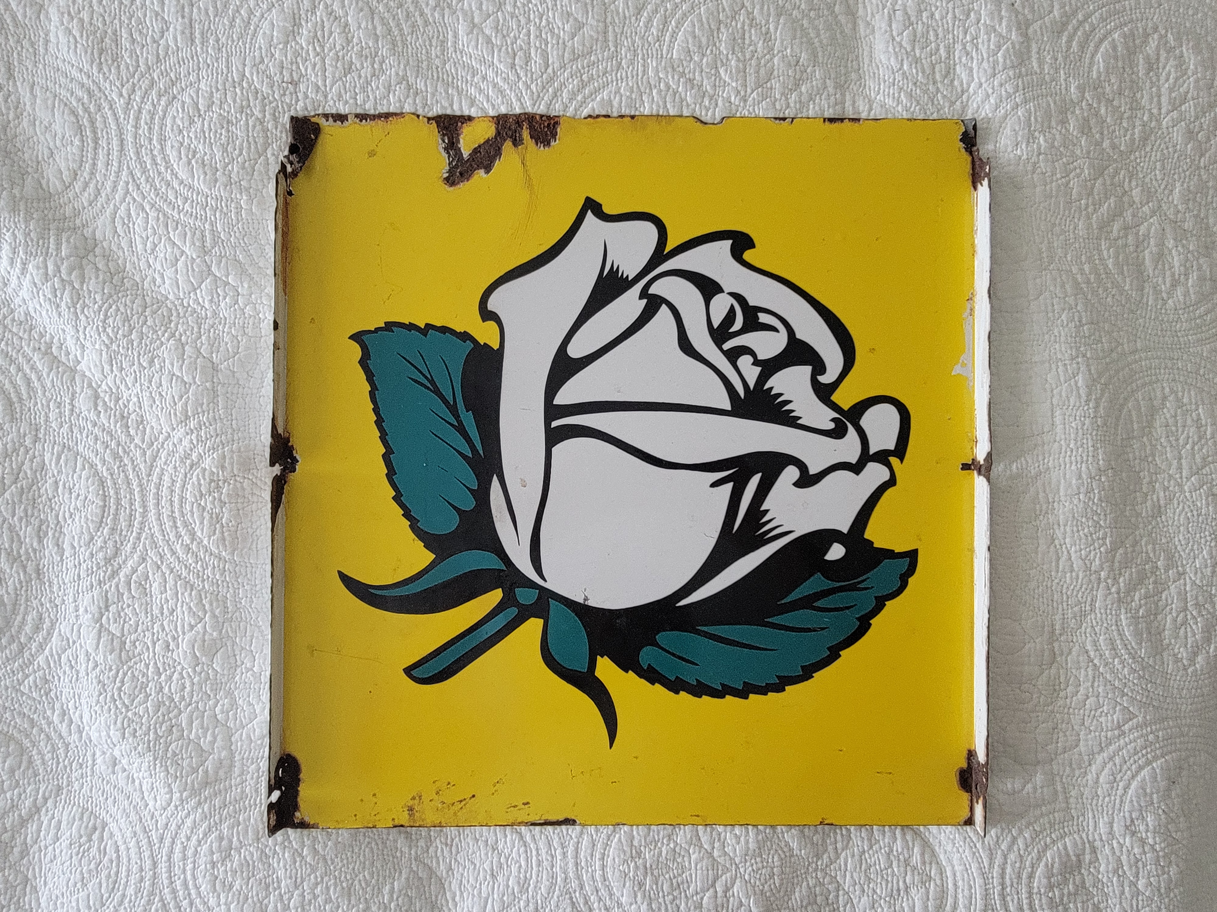 A stylized illustration of a white rose on a bright yellow background, with green leaves, displayed on a textured surface.
Double sided porcelain flange white rose gasoline side #1
vintage gasoline sign