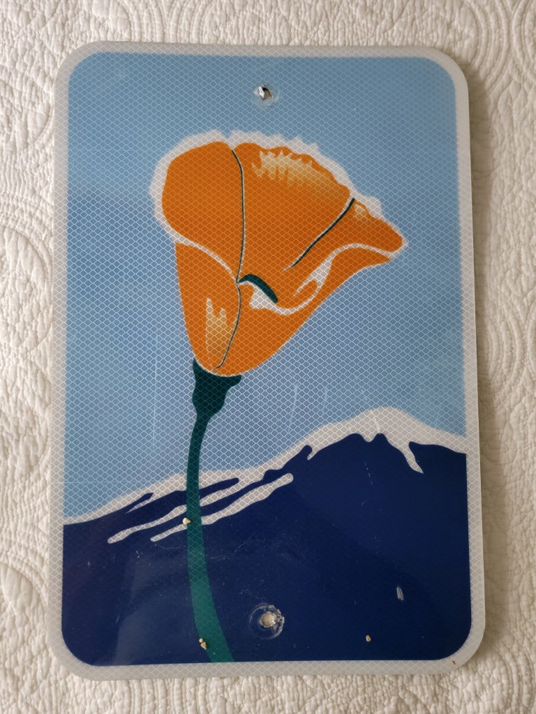 Illustration of a California poppy flower with an orange bloom and green stem, set against a blue background with a silhouette of mountains.
California PCH pacific coast highway poppy sign small street sign