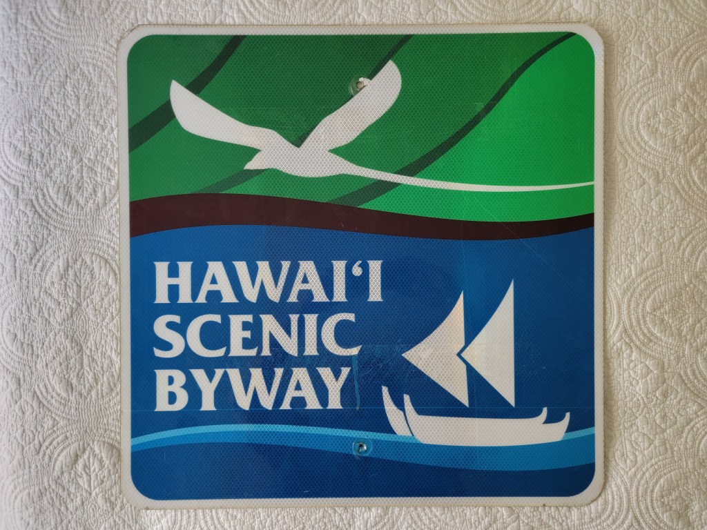 A colorful sign featuring the text 'Hawai'i Scenic Byway' with a design that includes a bird, waves, and a canoe.

Hawaii Scenic Byway Sign #2