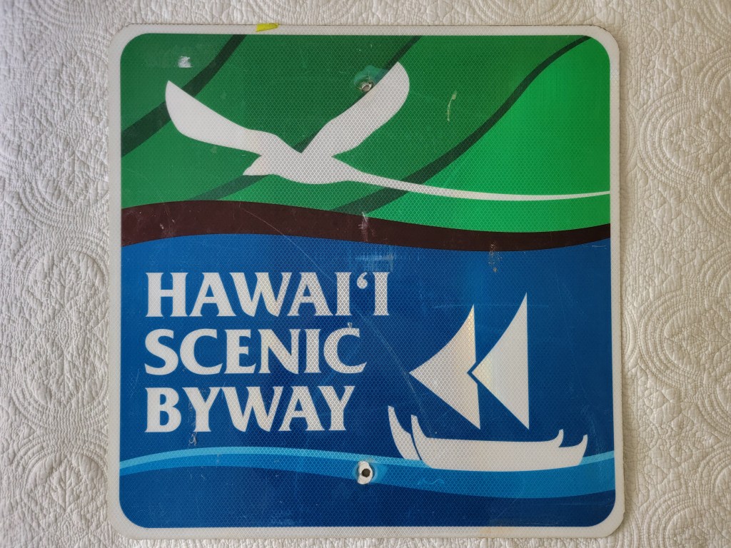 A sign indicating the 'Hawai'i Scenic Byway' with a design featuring a bird and a traditional Hawaiian sailing canoe.
Hawaii Scenic Byway Sign #1