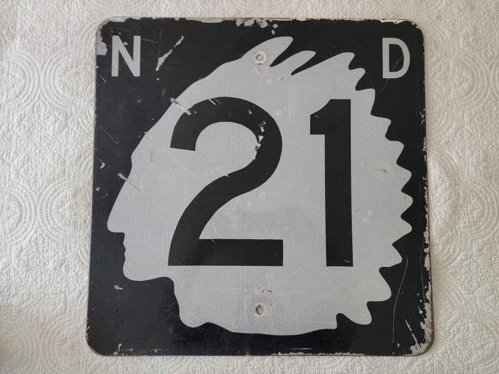 Old road sign displaying 'N 21 D' with a silhouette design.
North Dakota Indian chief street sign route 21