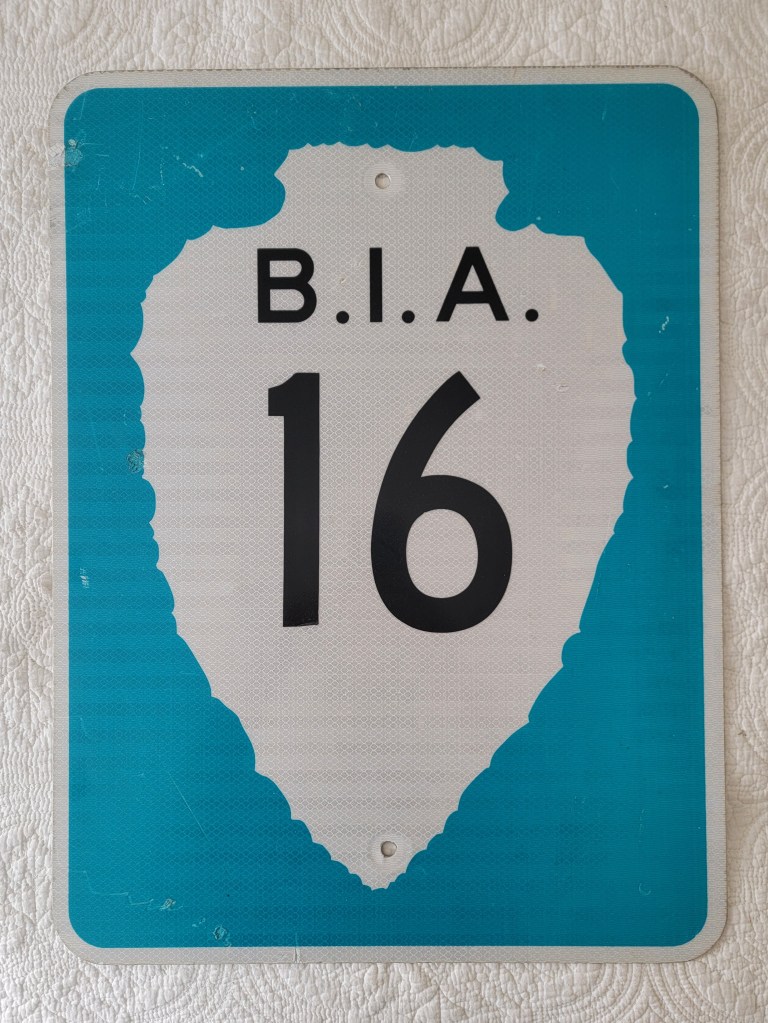 A blue and white road sign featuring the text 'B.I.A. 16' in large black numbers.
Bureau of Indian Affairs Arrowhead street route sign 2