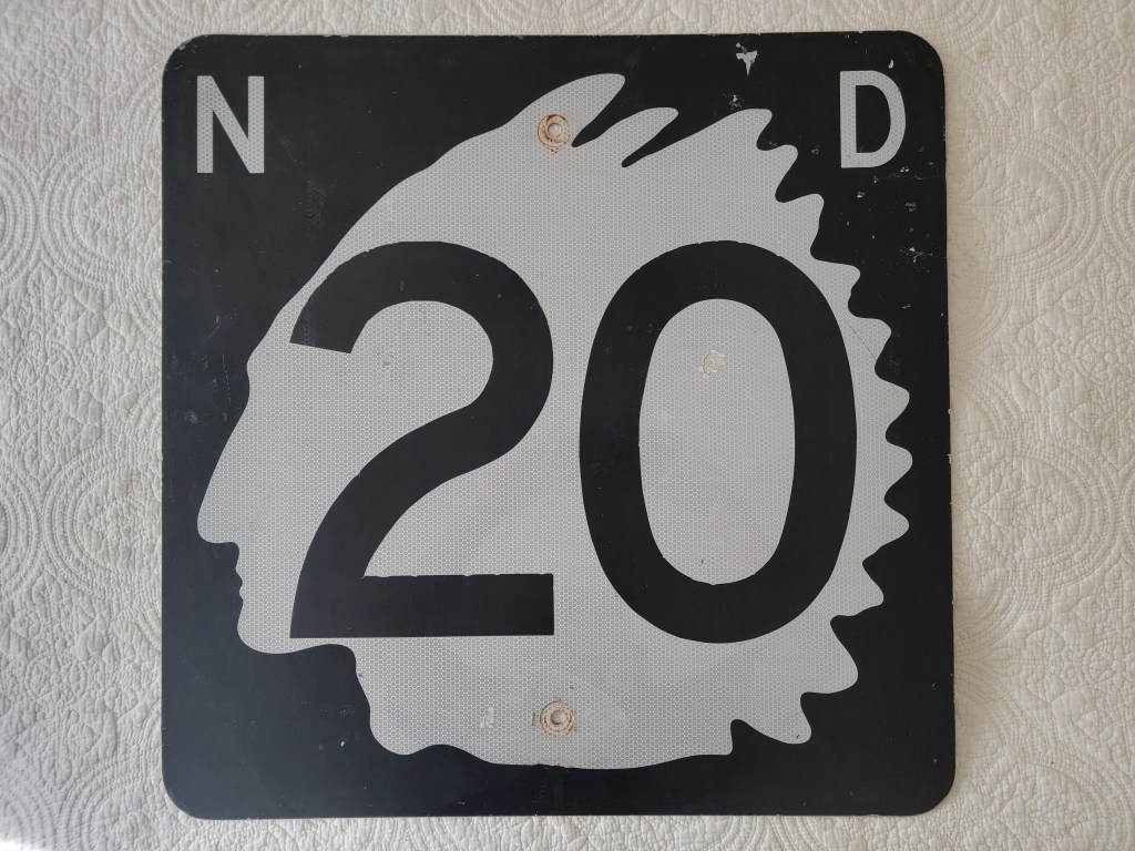 A black and white road sign featuring the number '20' and the letters 'N' and 'D' with a stylized head silhouette in the design.
North Dakota Indian chief street sign route 20