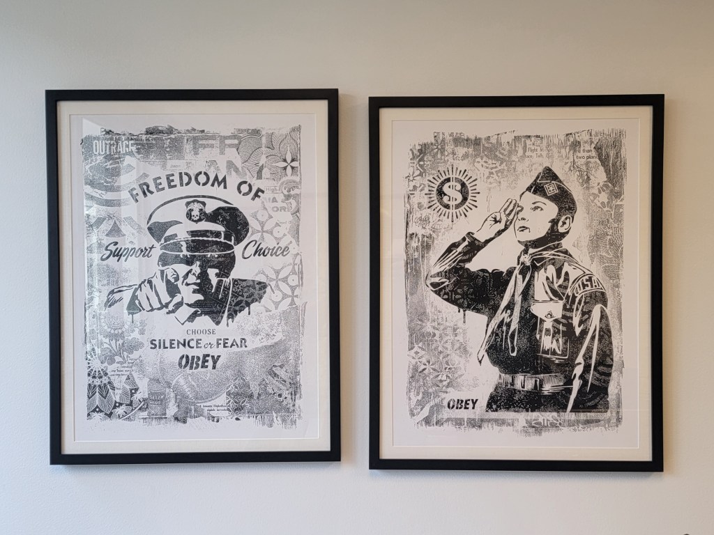 Two framed artworks on a wall. The left artwork features a police officer with the text 'Freedom of Support Choice' and 'Choose Silence or Fear OBey'. The right artwork depicts a young soldier saluting with the text 'OBEY'. Both are in black and white.

Shepherd Fairey Obey
Choose silence or fear, 2017
serigraph on paper

Learn To Obey (Damaged Stencil Series)